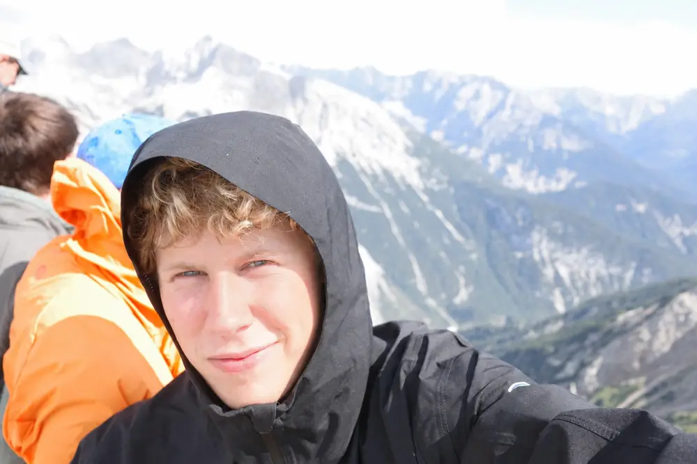 Liam Gergen in a black hood, with mountains behind him